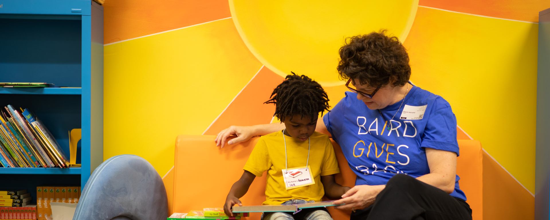 Woman in a SilverPeak Strategic Capital Cares t-shirt reading to a student.